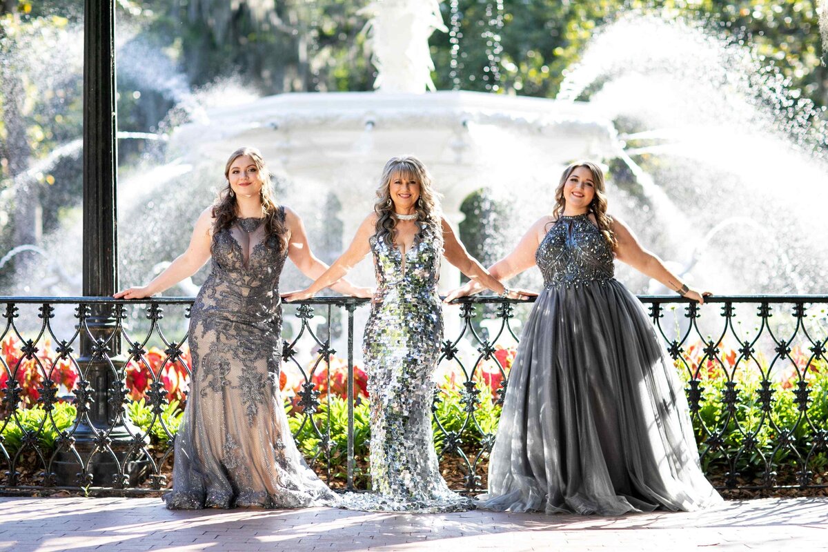 mother and daughters in gowns posed in front of fountain