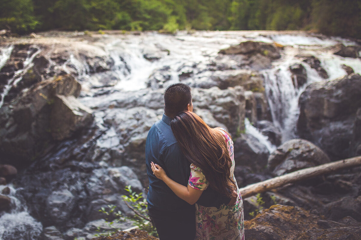 A couple gazing at a waterfall during their Vancouver Island engagement photos.