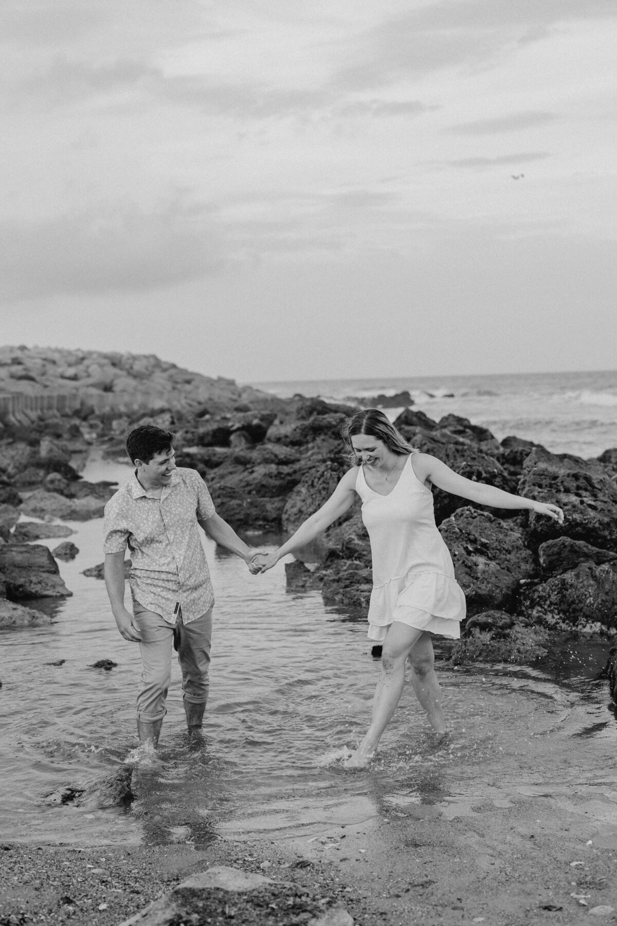 Couple stomping in shallow water, playful Wilmington beach engagement session