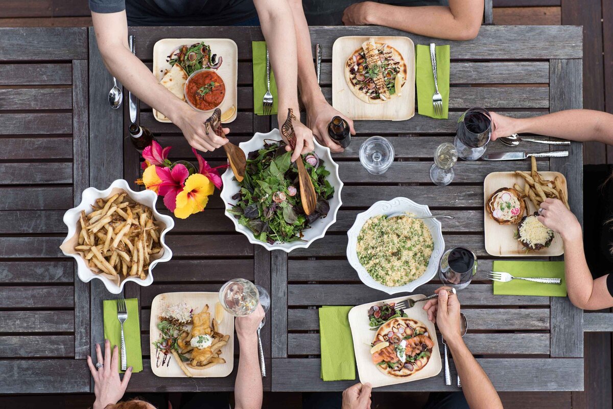 A sot looking down at a picnic table with hands serving and eating and drinking food. Marketing for a food delivery company