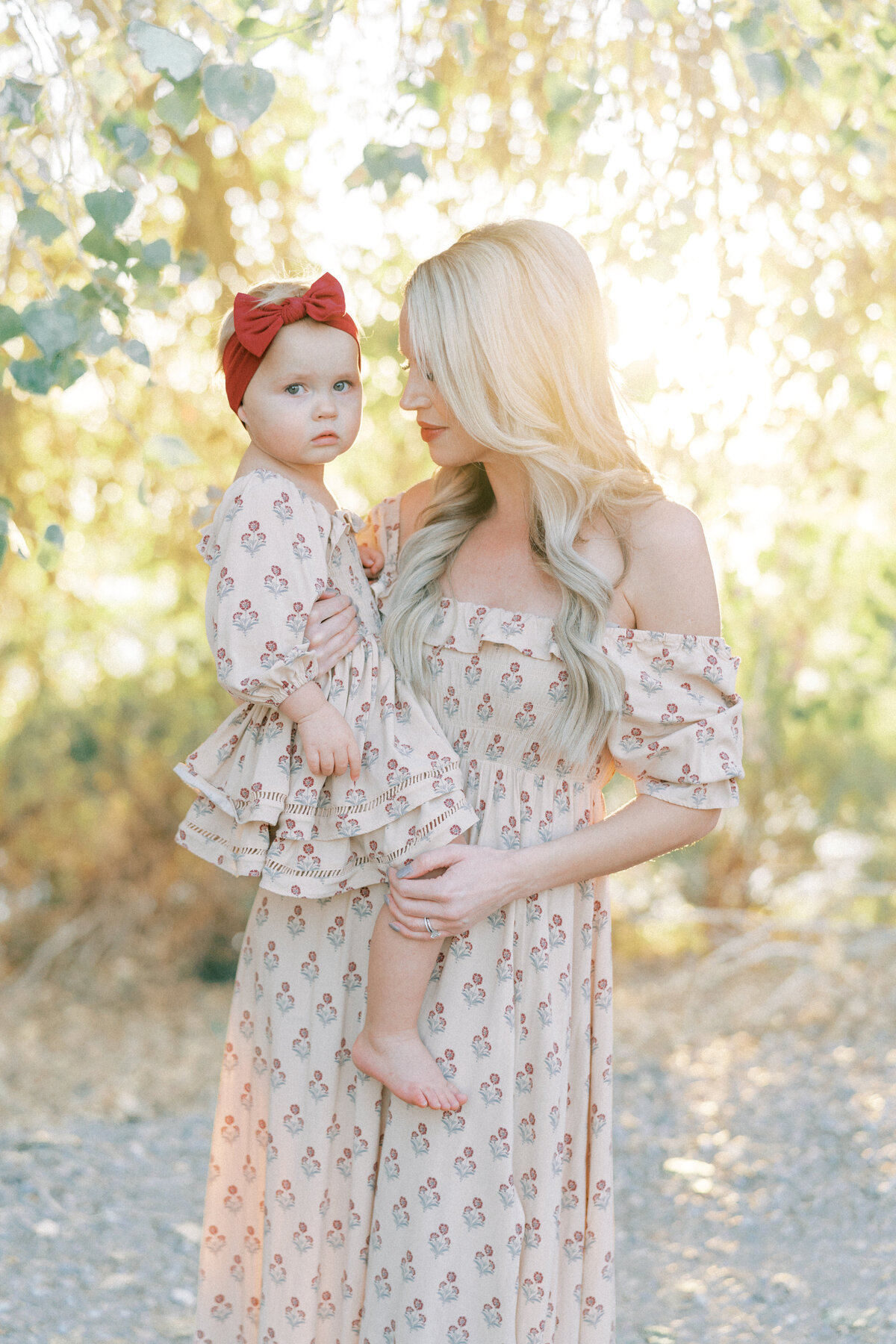 mom in pink dress holding daughter in pink dress.