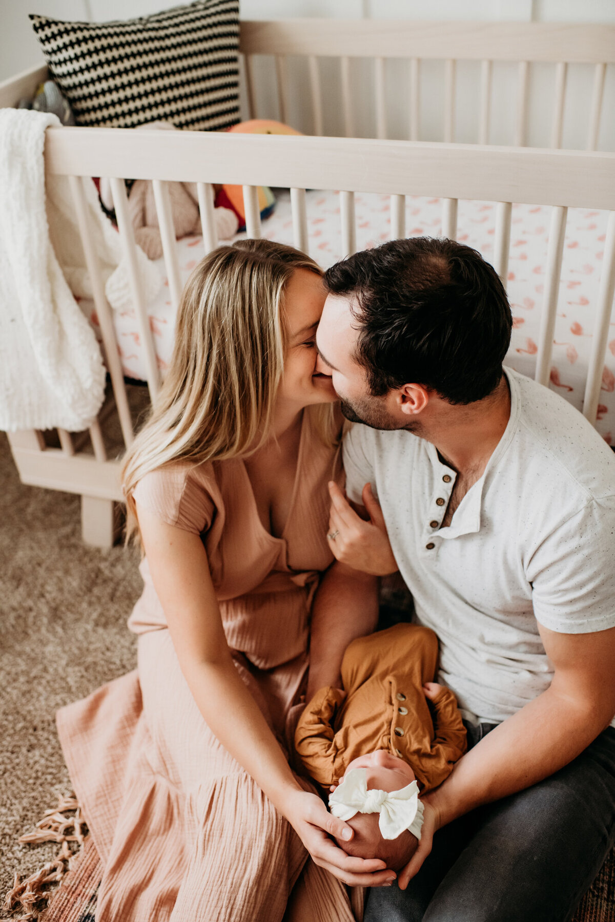 Newborn Photographer, Mom and dad kissing in front of the crib while holding their baby girl.