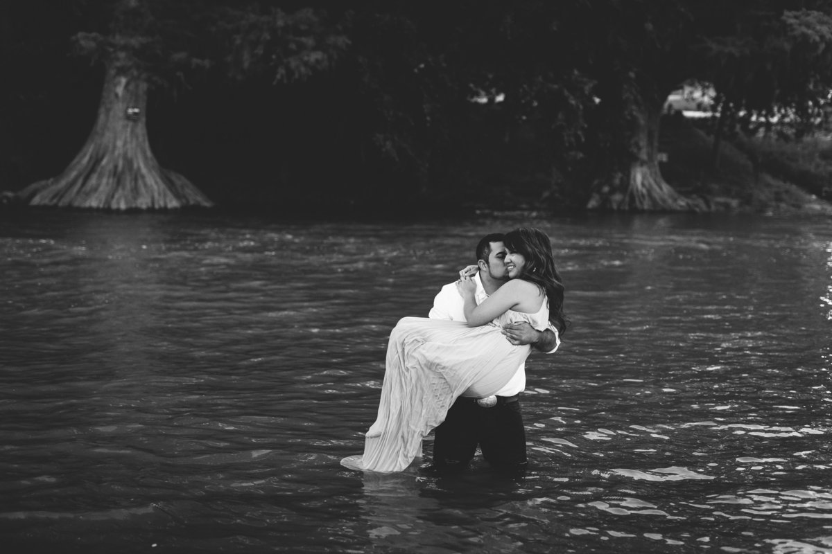 Man carrying a women while standing in a river while on their engagement session with Expose The Heart Photography.