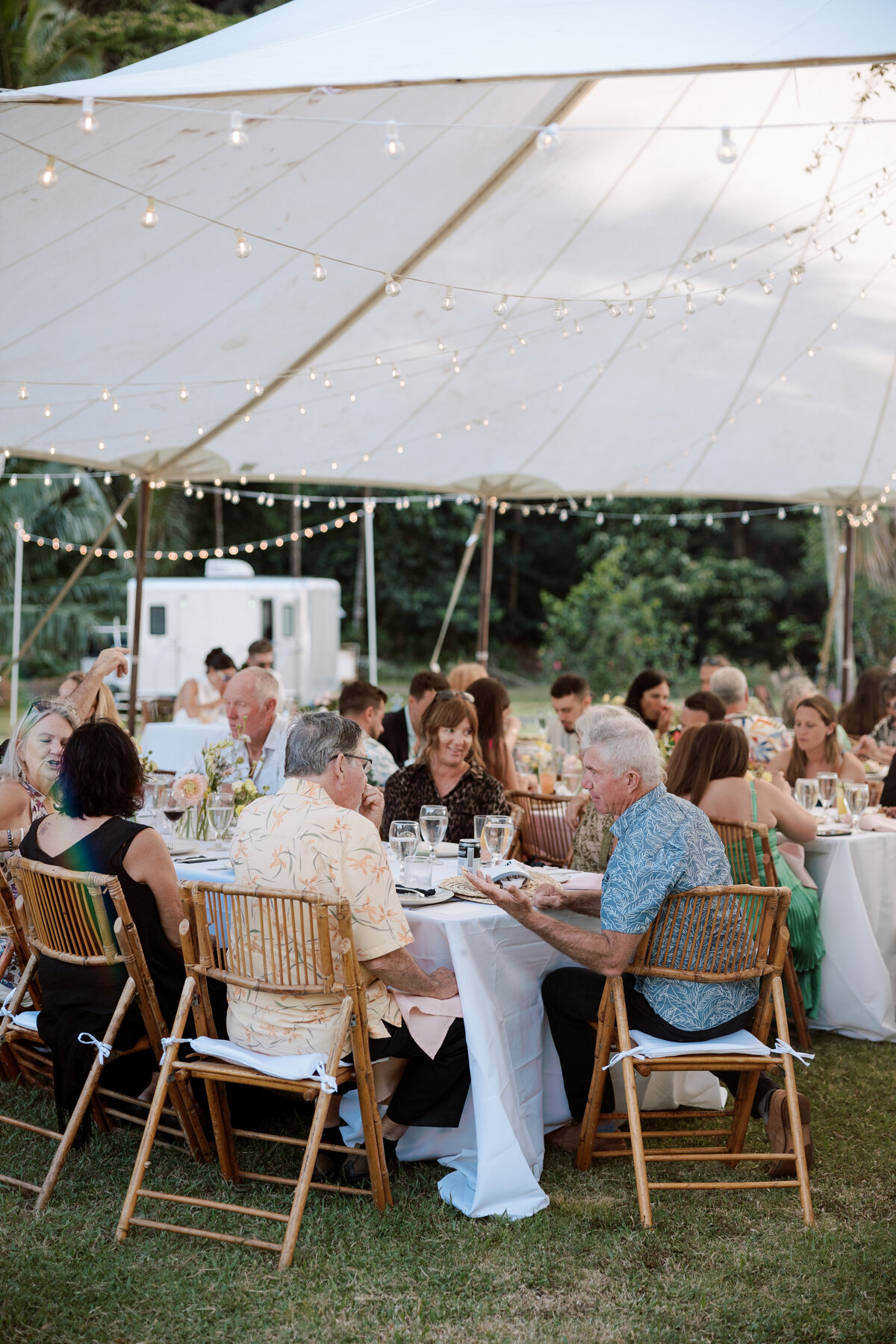 Older man chatting during a wedding reception, with a marquee and tropical flowers, captured in a candid wedding photography style — Carmel wedding photography by Kate Winters Photography.