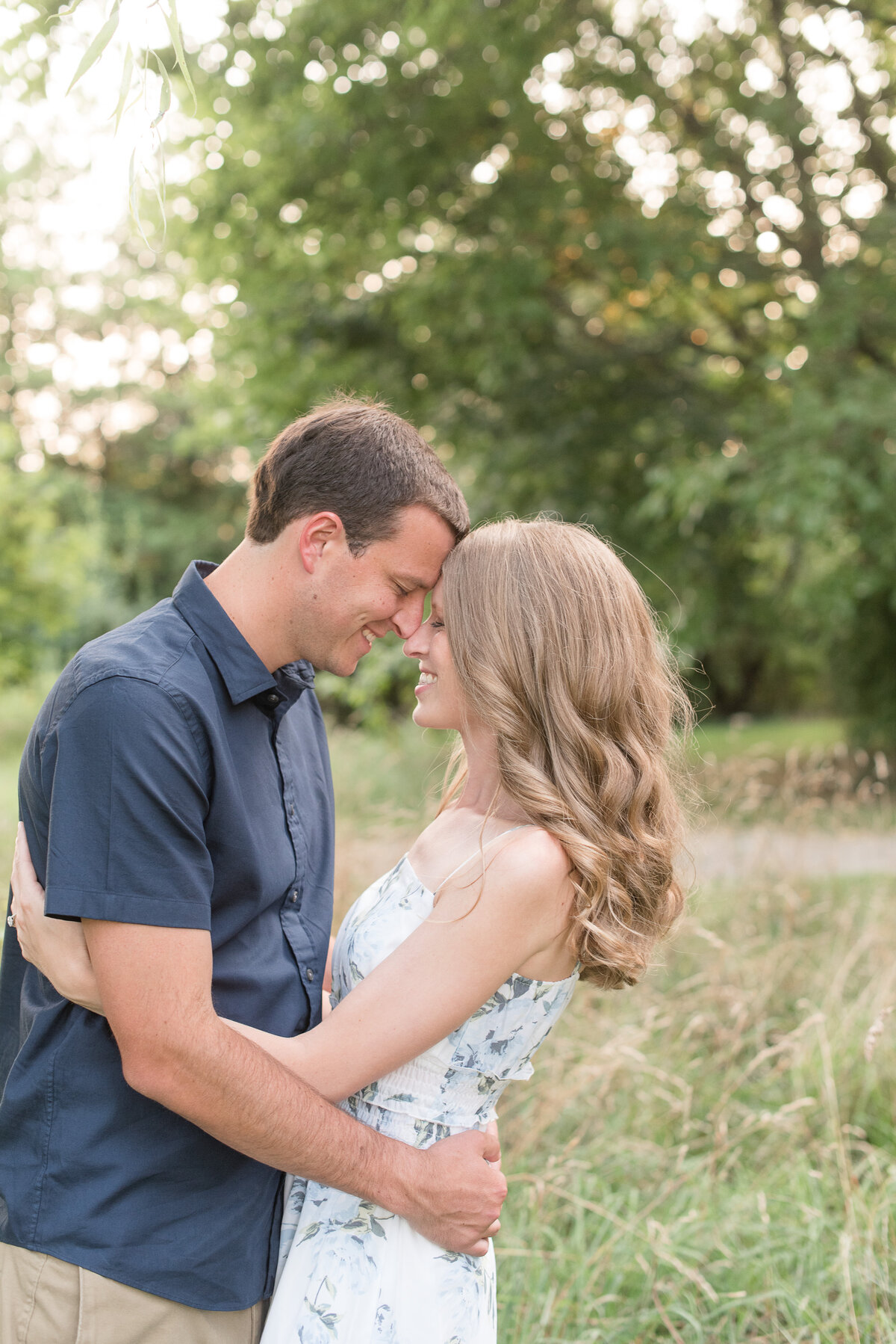 Engaged couple hugging and resting their foreheads together as they smile among tall wild grasses.
