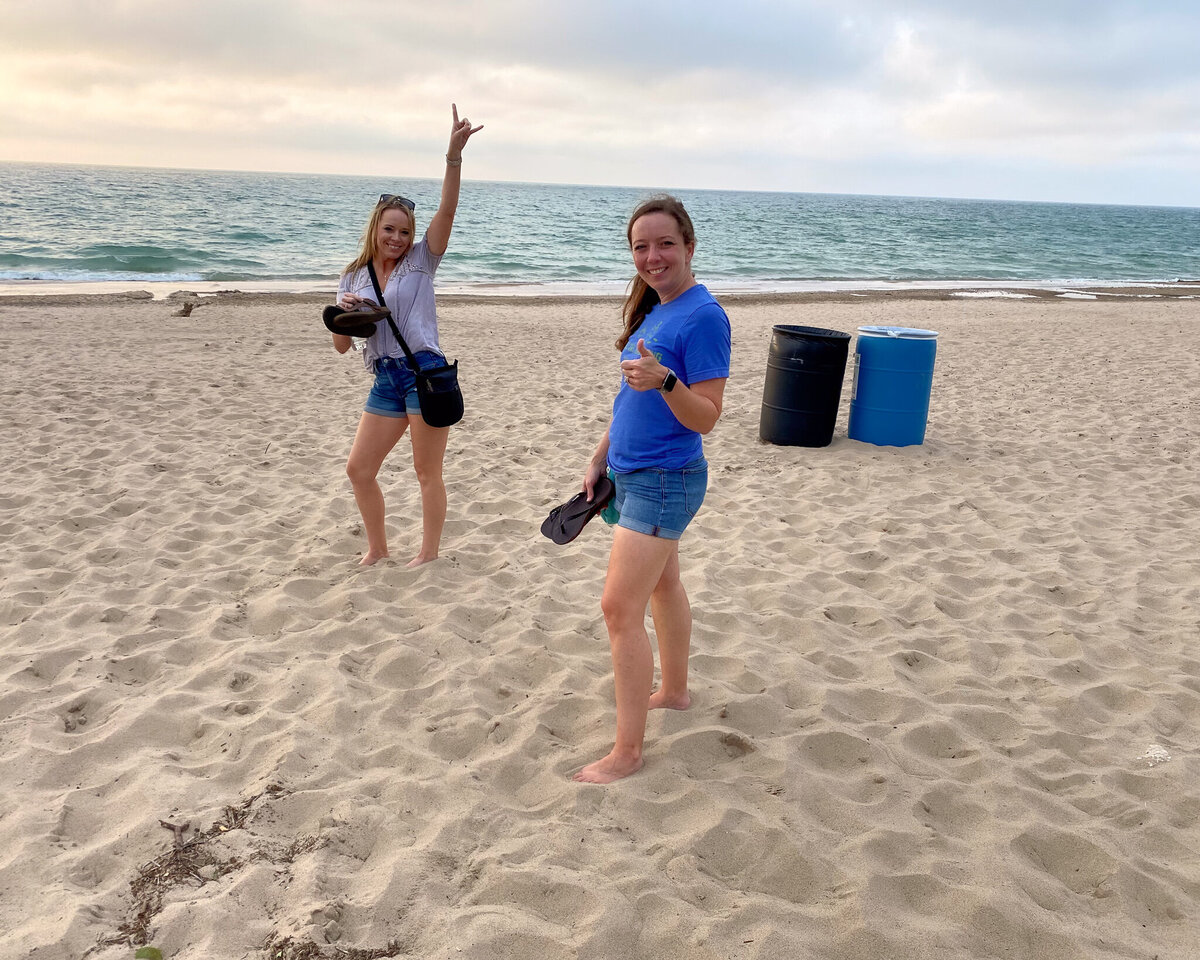 sisters standing on the shore with the lake behind them giving a thumbs up and smiling at the camera