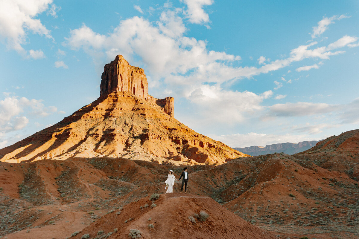 A bride and groom stand in the shadow of a red rock formation on their elopement day. 