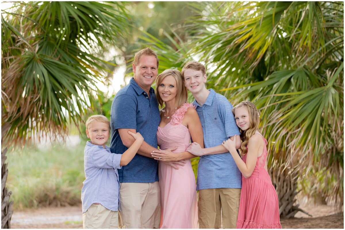 Beautiful family in pinks and blues hugging with palm trees in the background