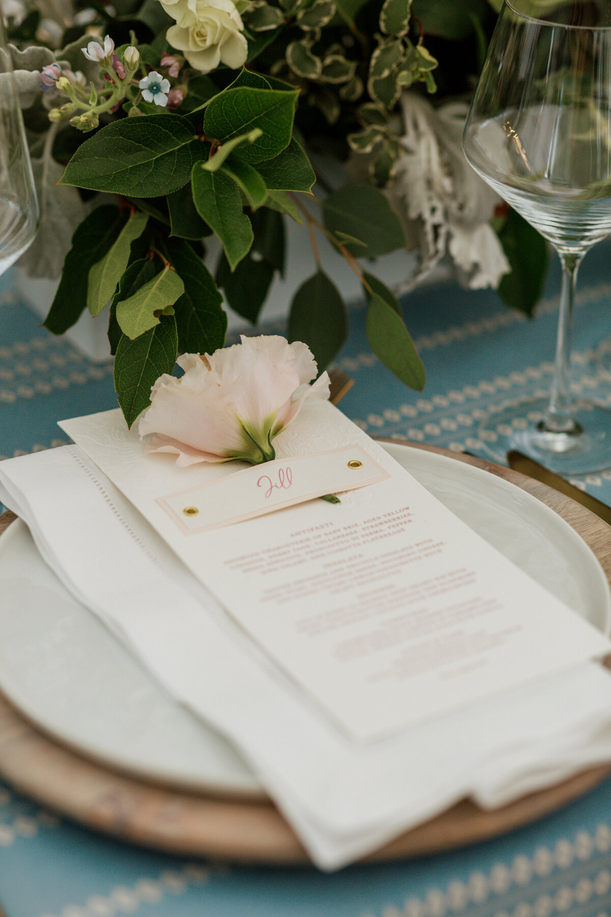 a custom wedding stationery design featuring a wedding dinner menu with a custom name tag and a flower on it on top of a white plate from alyssa amez design