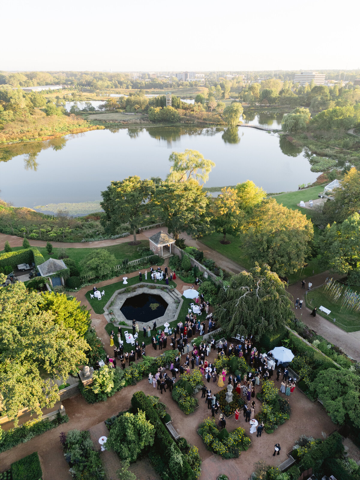 Aerial view of an outdoor wedding ceremony in a lush garden by a lake at the Chicago Botanic Gardens.
