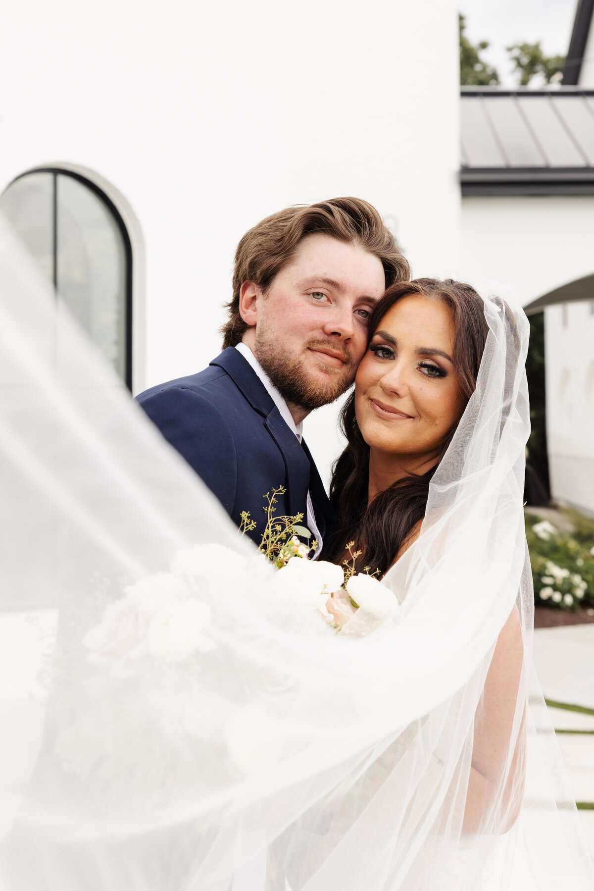 Close-Up of Bride and Groom Holding Bouquet Under Veil Smiling