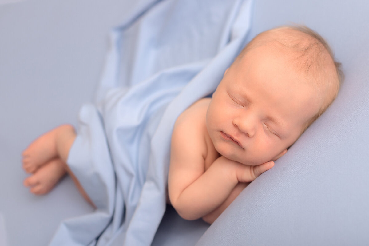 nyfödd bebis poserad på sidan med blå wrap och matchande blå bakgrund