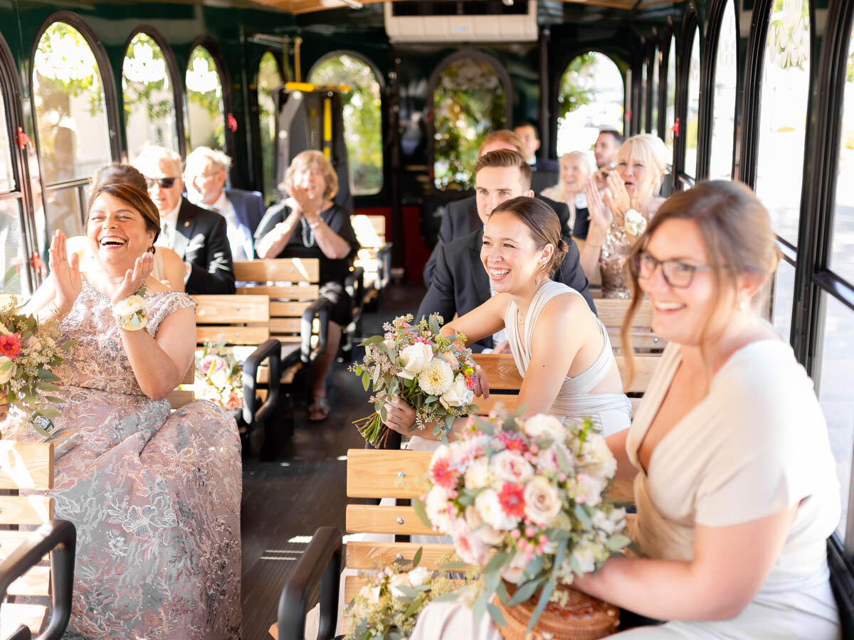 Members of the wedding party and family cheer as the newlyweds join them on the trolley.