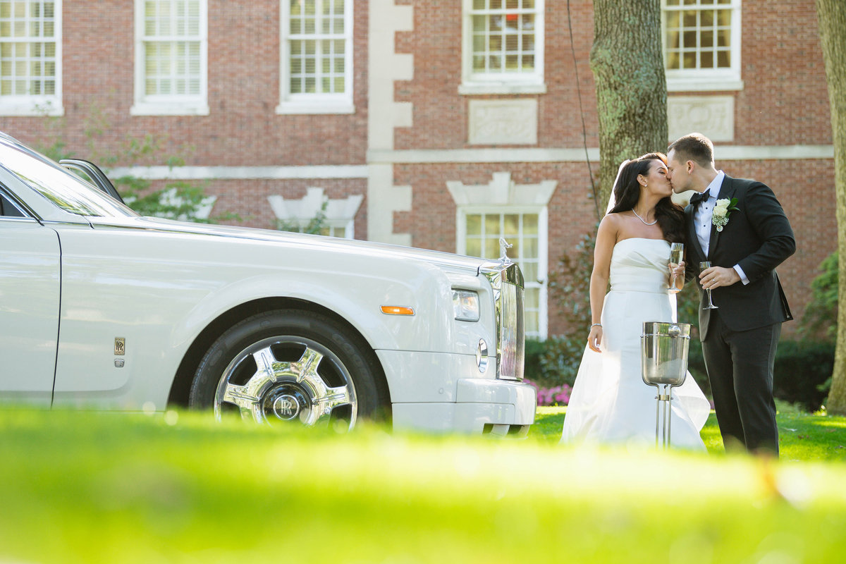 bride and groom kissing in front of car and main clubhouse mansion at The Muttontown Club