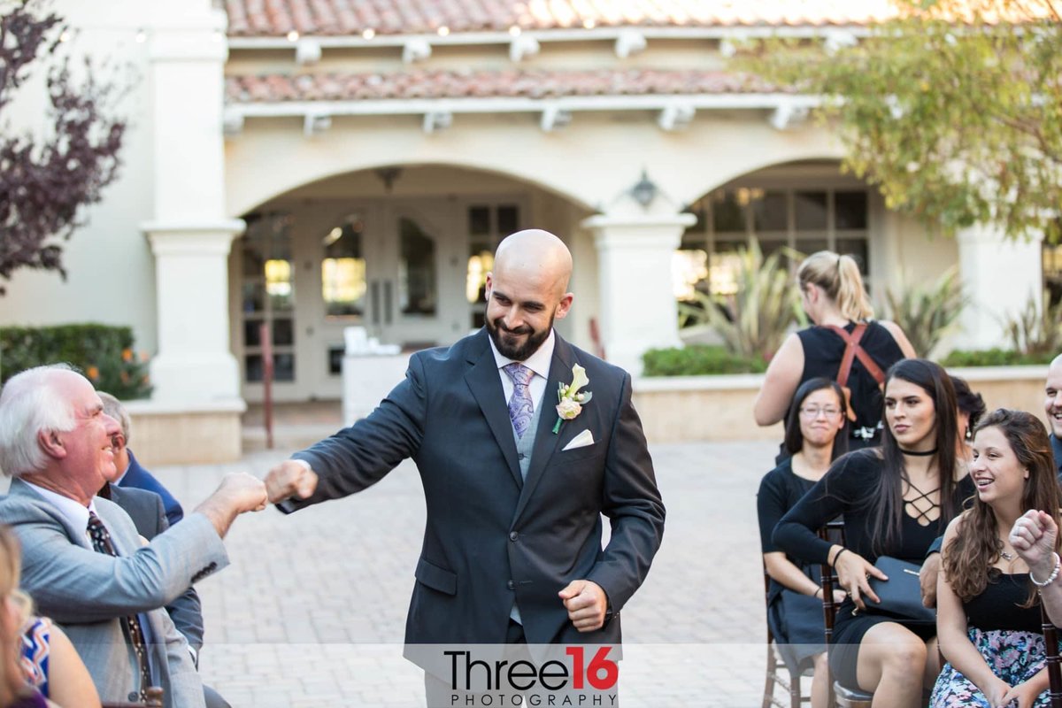 Groom fist bumps wedding guest as he walks up the aisle