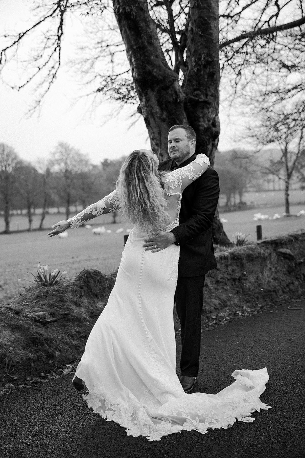 A couple dancing on a road lined with trees, the bride's white dress trailing behind