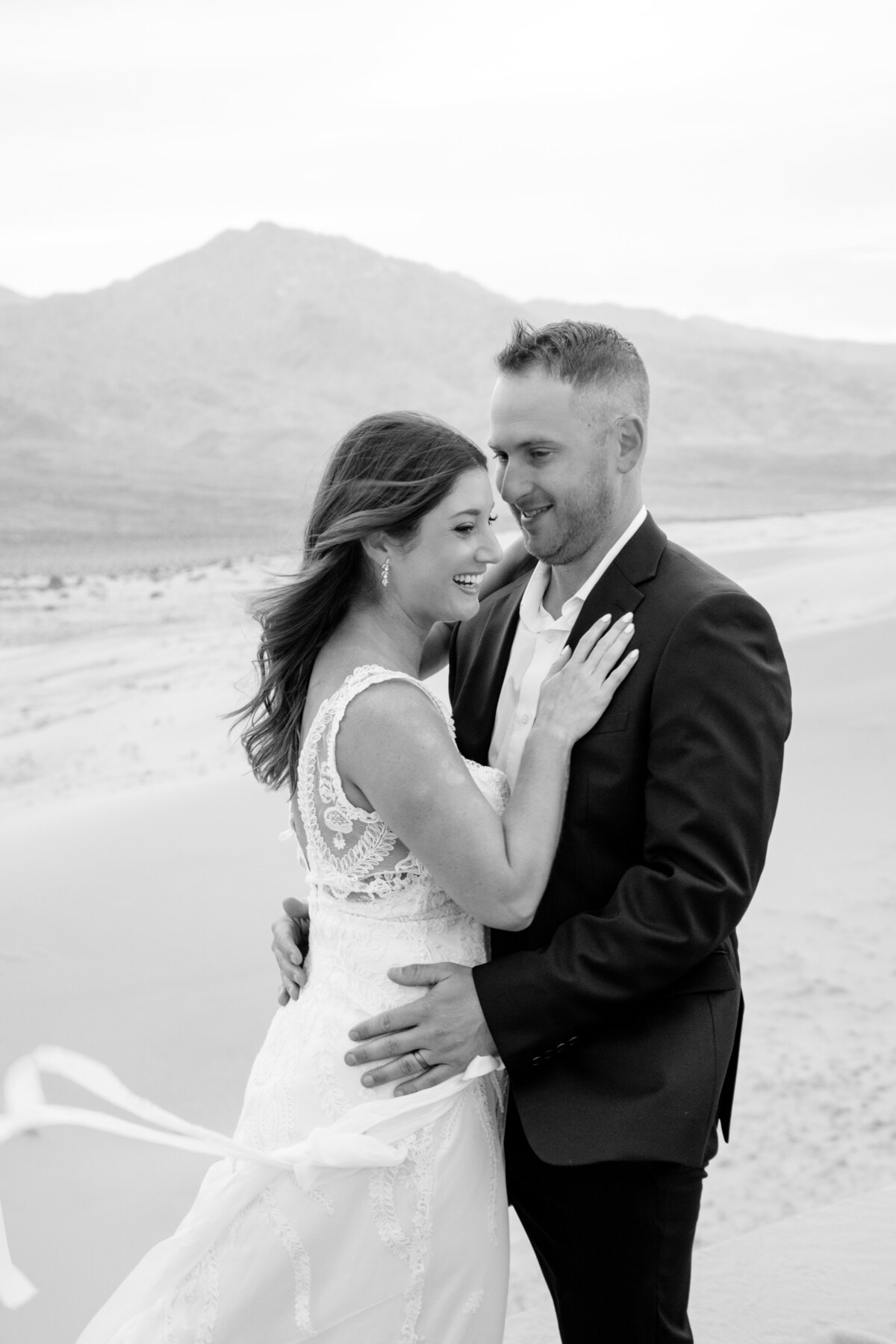 Black and white portrait of bride and groom at Kelso Dunes at sunrise holding each other laughing