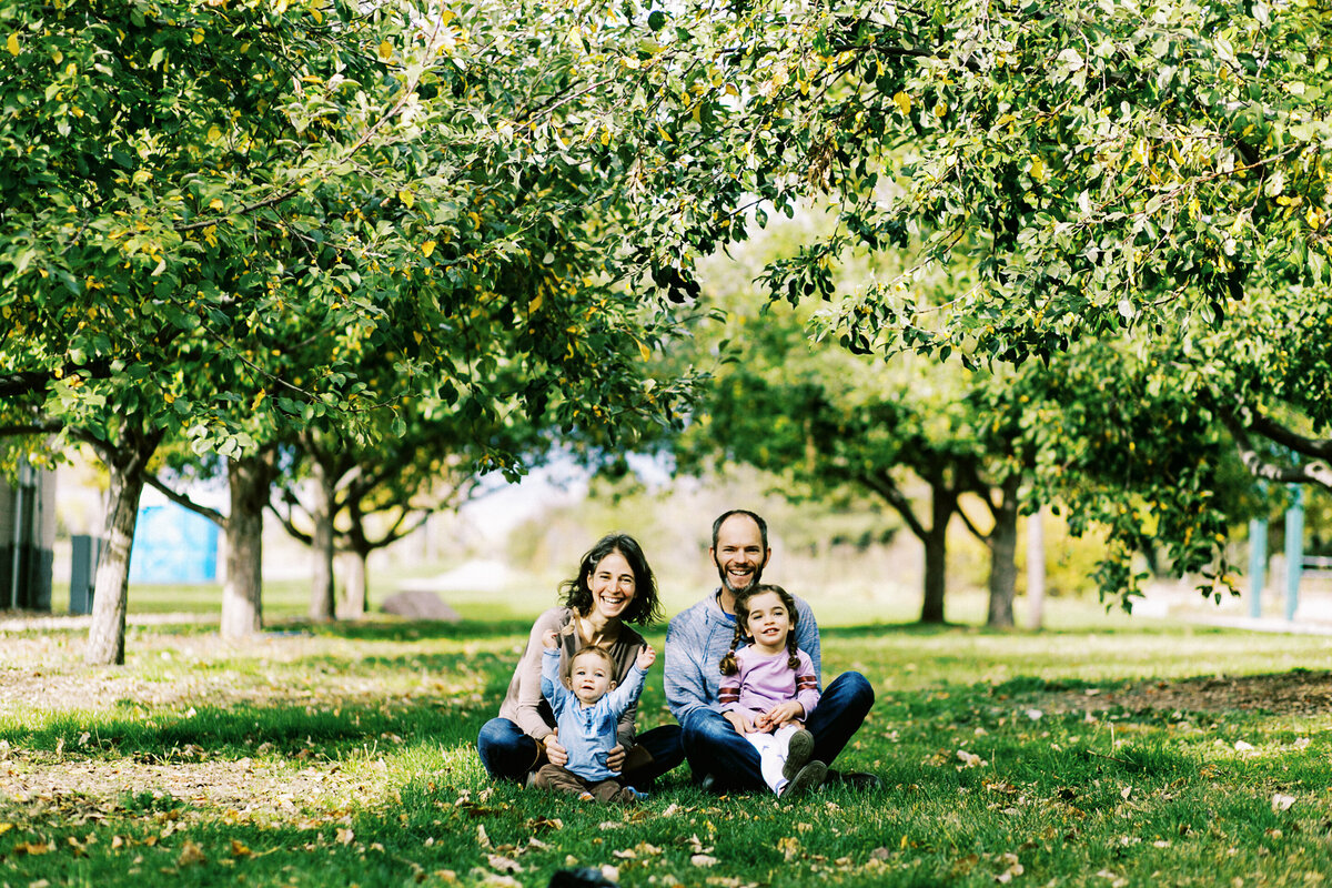 family sits under apple trees in longmont, colorado