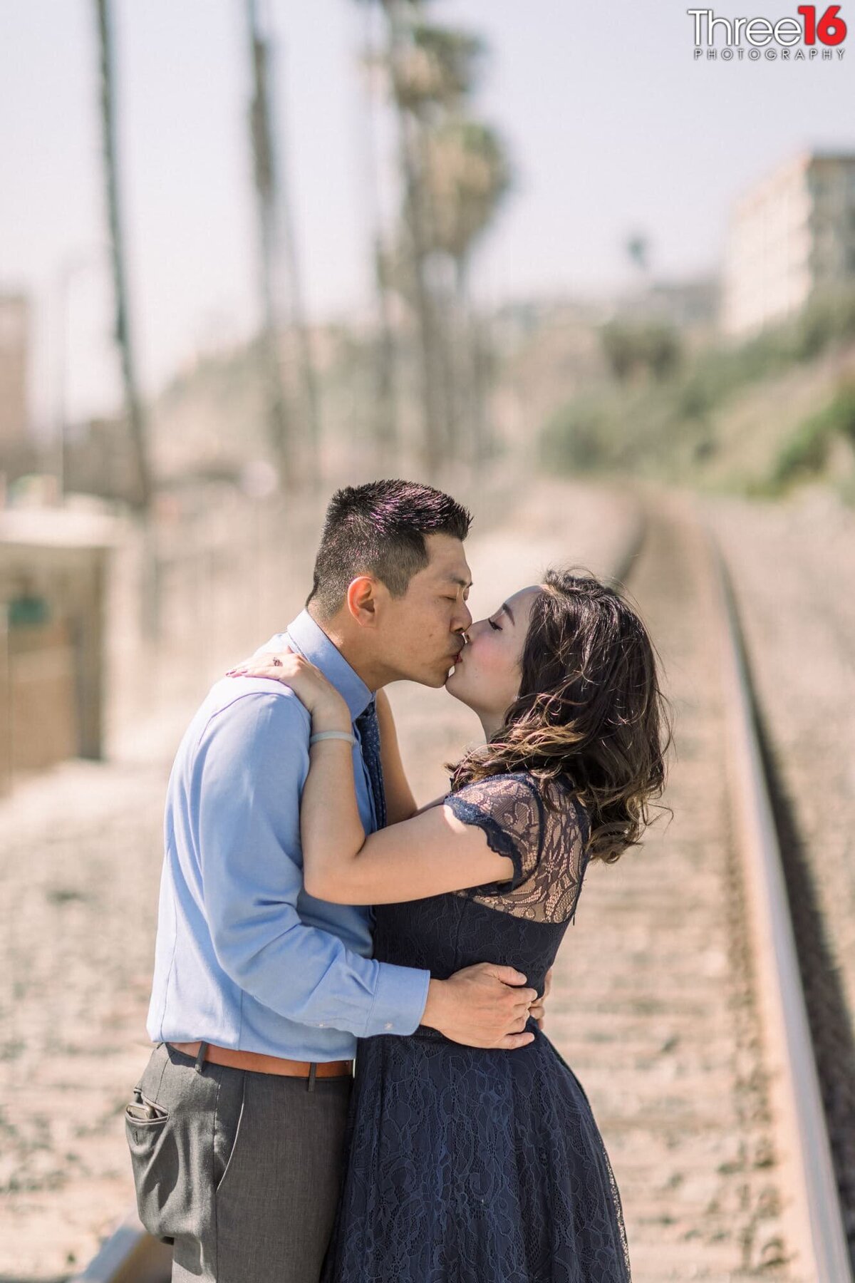 Standing on the San Clemente Pier train tracks engaged couple embrace in a kiss