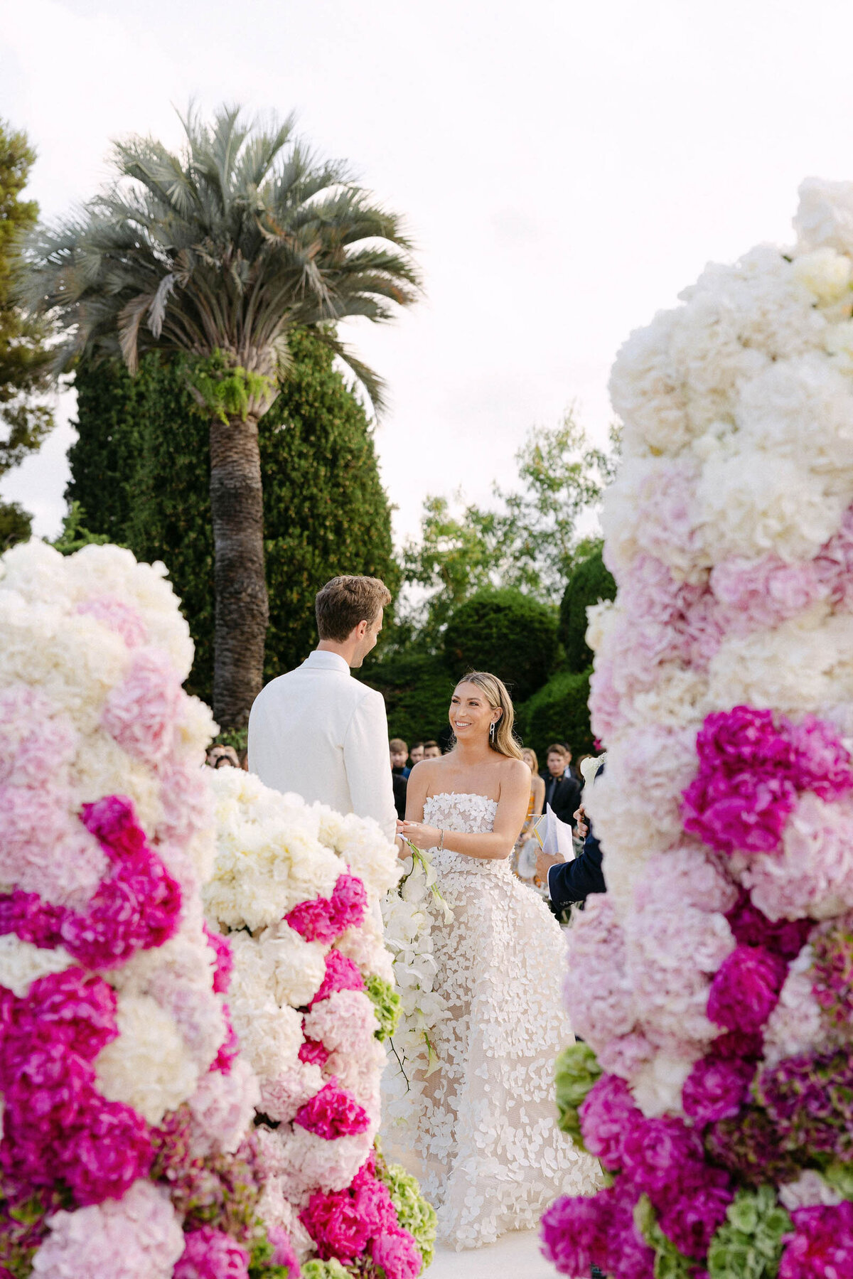 Bride and groom exchanging vows surrounded by white and pink floral installations.