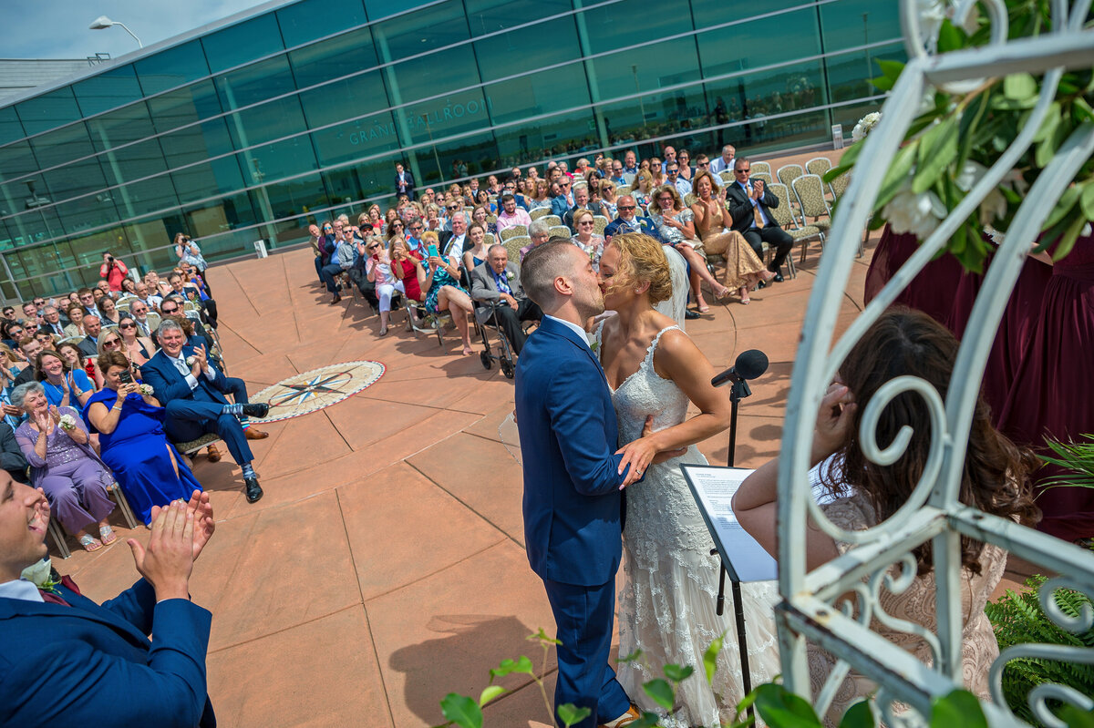 Bride and groom kiss in front of crowd during wedding ceremony at Bayfront Convention Center Erie.