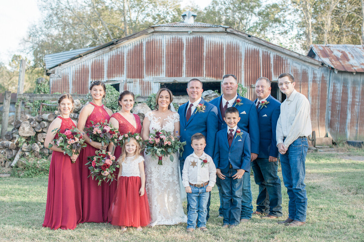 The wedding party gathers to smile for the camera in front of a rusted metal barn