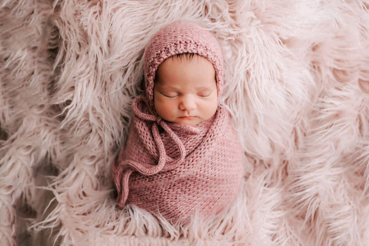 portrait of newborn baby girl wrapped in pink blanket and laying on fuzzy rug that is pink