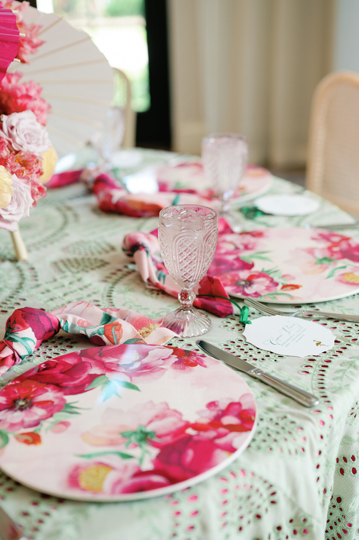 A beautifully curated table setting featuring delicate pink floral plates, silver utensils, and sparkling crystal glasses. The soft color palette and refined details create a sophisticated and romantic dining experience, perfect for an elegant wedding reception or luxury event.