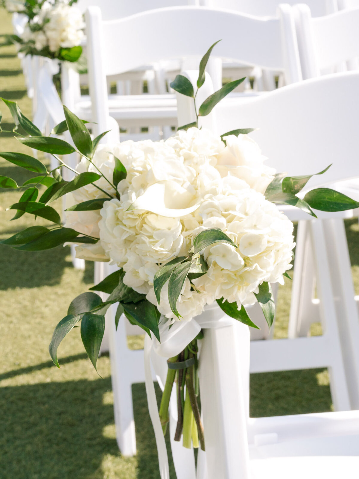 White floral arrangement tied to a ceremony chair at an outdoor wedding at Lido House