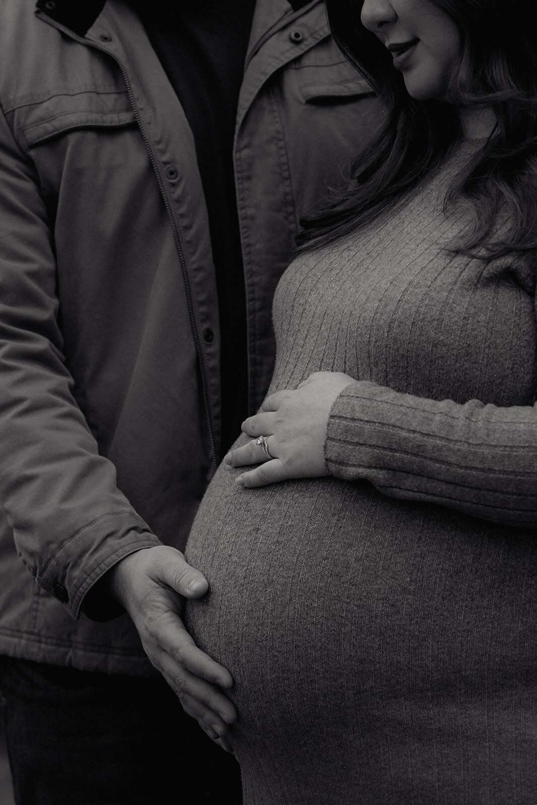 A black-and-white maternity portrait highlighting hands on a baby bump, captured in a fine art wedding photography style.