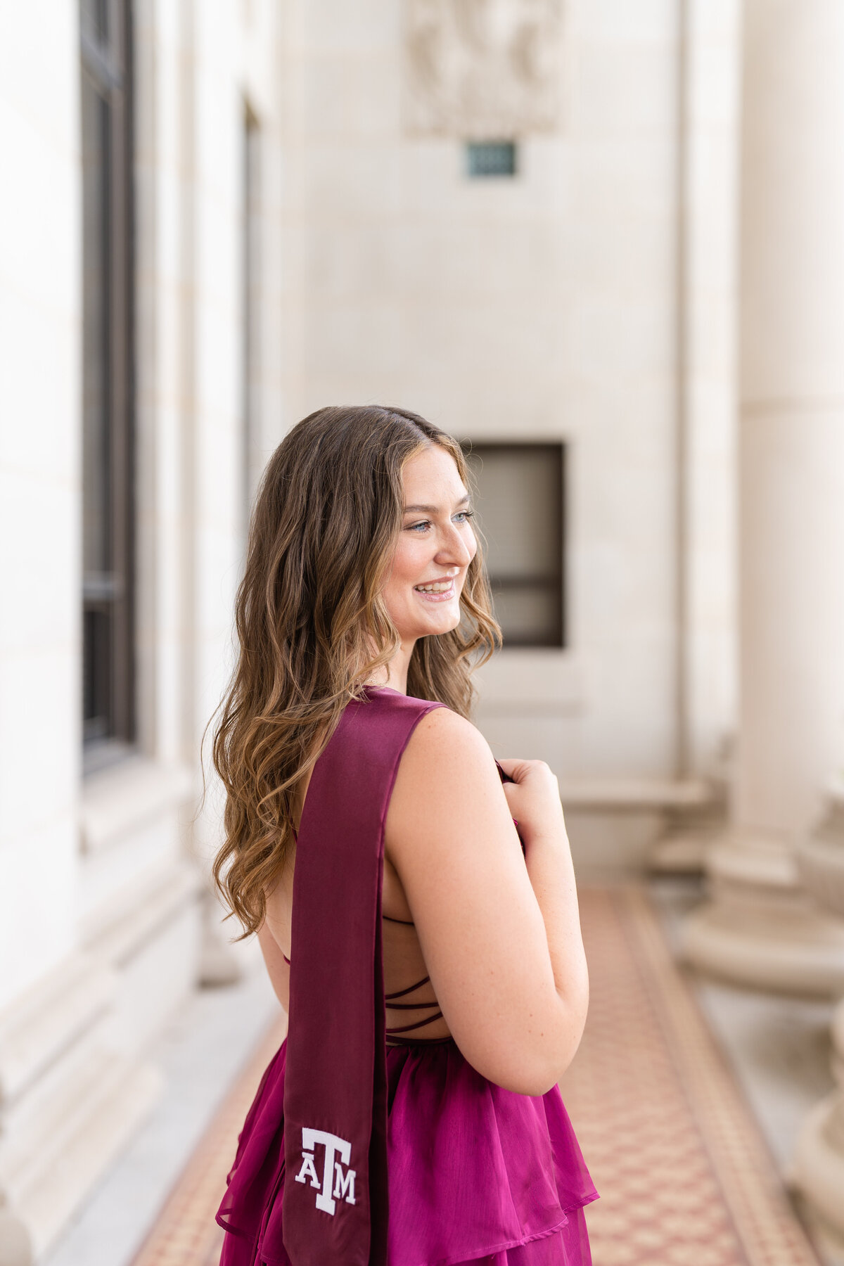 Texas A&M senior girl holding stole over shoulder while looking away and wearing maroon dress in the columns of the Administration Building