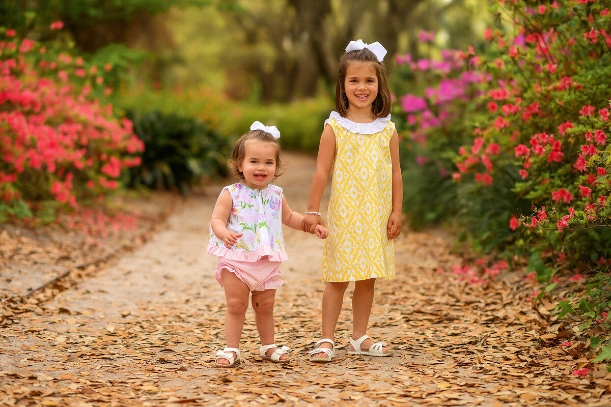 Sisters hold hands among azalea blooms in Hampton Park during their Family Photos in Charleston, SC.
