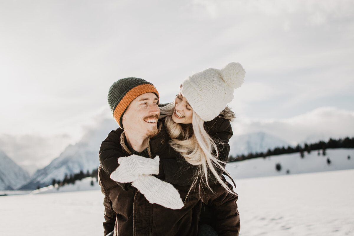 jackson hole engagement photos with woman leaning over mans shoulder  while holding him and smiling as they look each other in Jackson Hole Wyoming