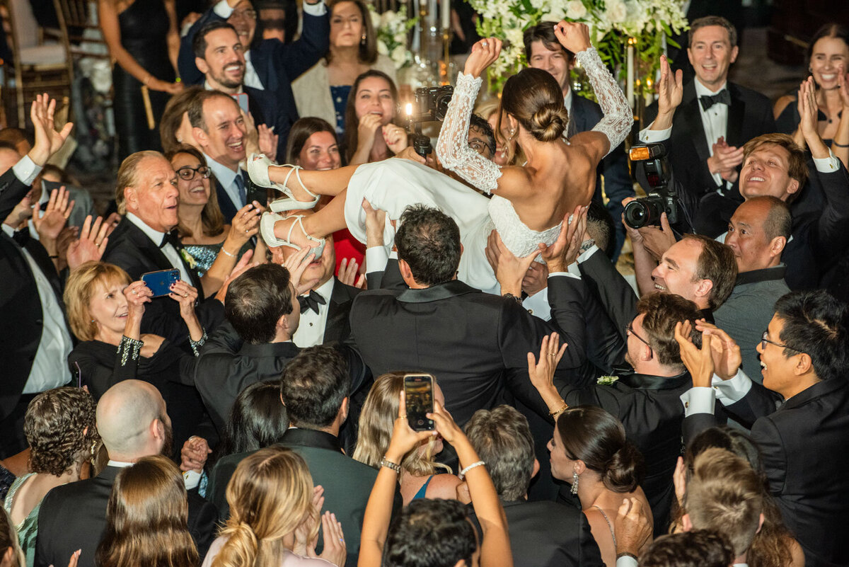 A man is carrying a bride in his arms in a crowd of people