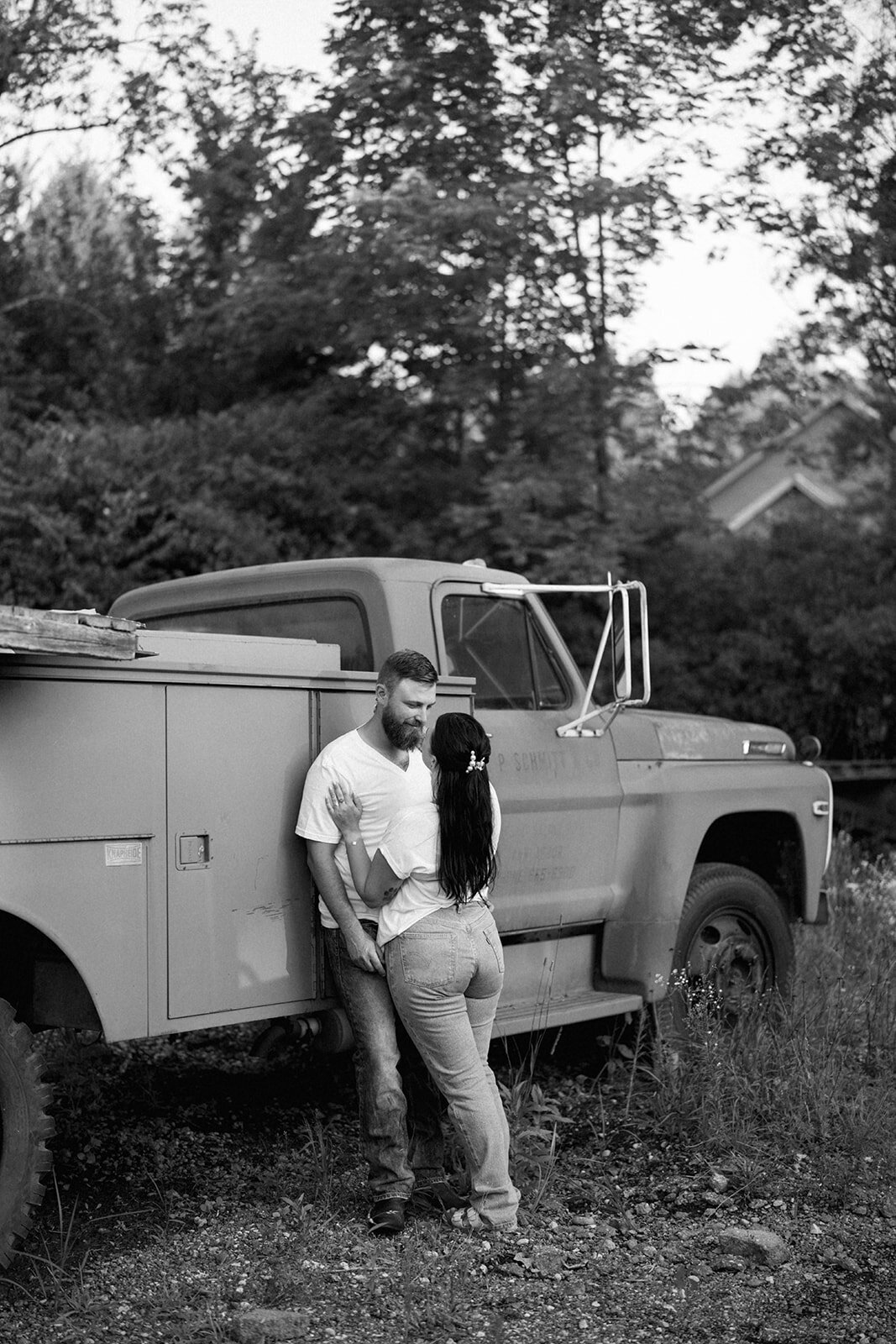 Black and white photo of Kali and Joe kissing beside an old pickup truck during their Detroit engagement session.