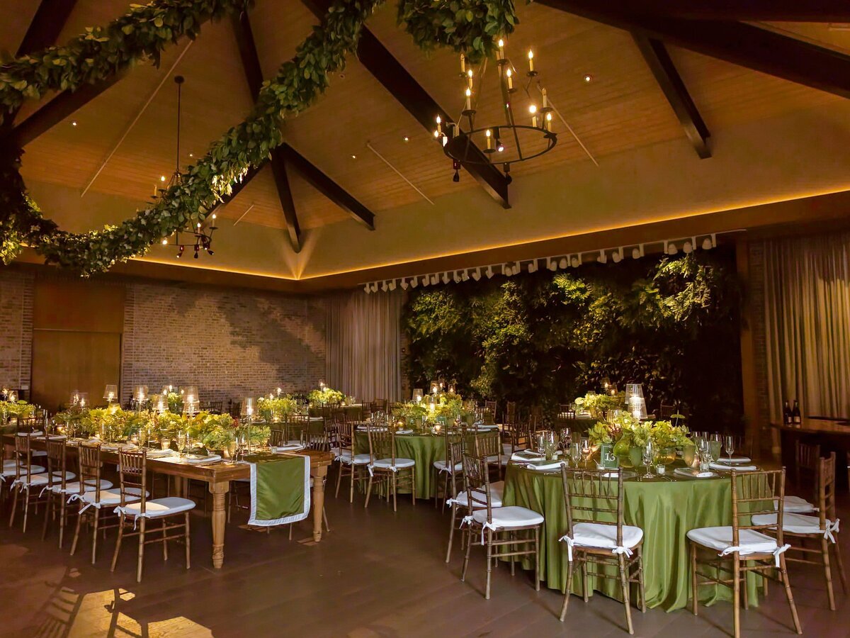 The reception room at Pendry Natirar with farm tables, green linens and smilax garlands across the beams