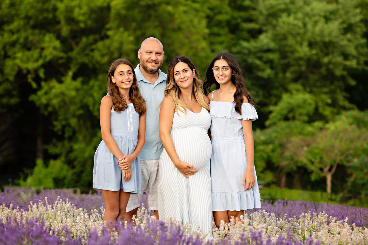 mom and dad with their teen daughters standing in a lavender field for their summer maternity photography session in Burlington, On