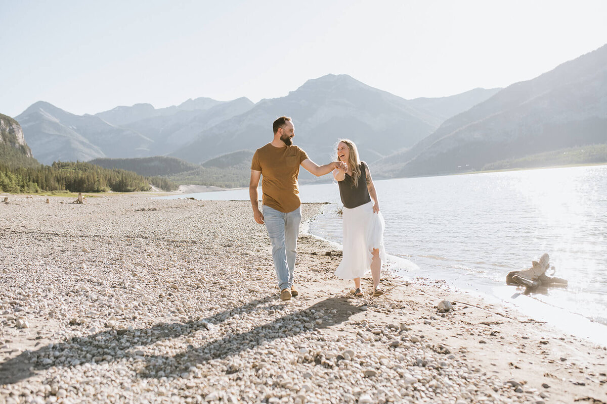 Couple-walking-beach-mountains-behind-them