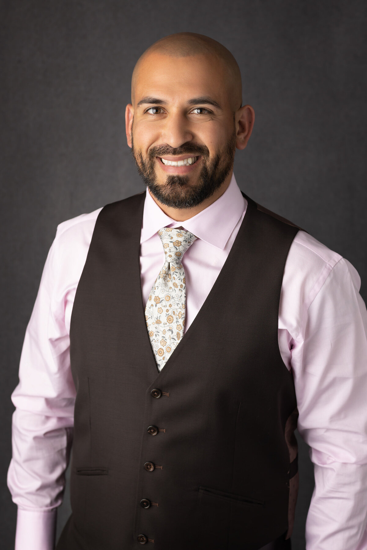 A Dallas family photographer captures a professional portrait of a father in a pink shirt and brown vest, smiling warmly for the camera.