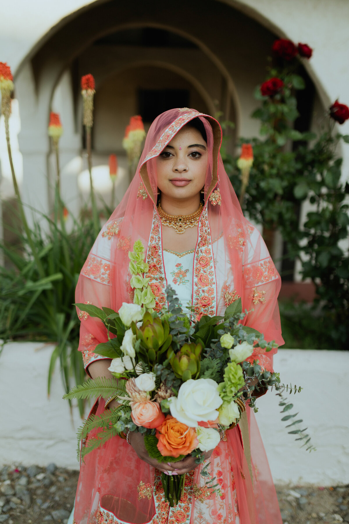 Indian Bride wearing read lehenga and dupatta holding vibrant bridal bouquet during bridal session in reno nevada