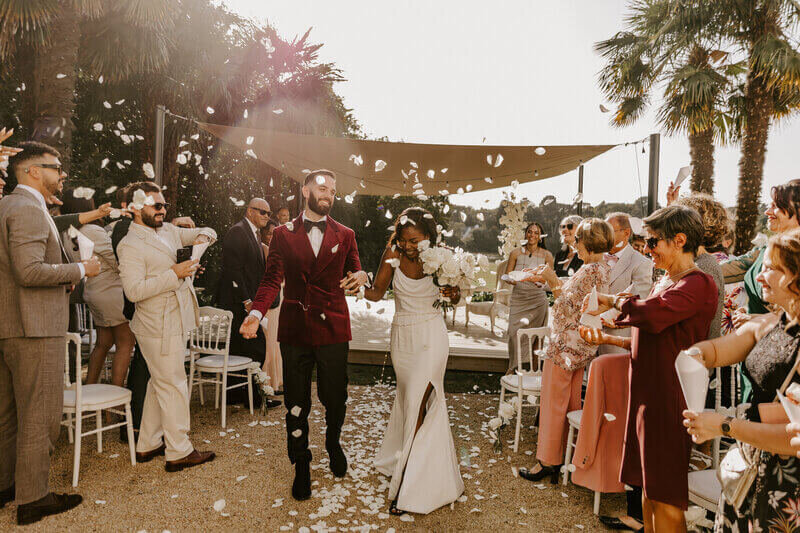 Sortie des mariés après la cérémonie laïque et recevant des pétales de fleurs de la part des invités formant une haie d'honneur pour la séance photo mariage en Vendée.