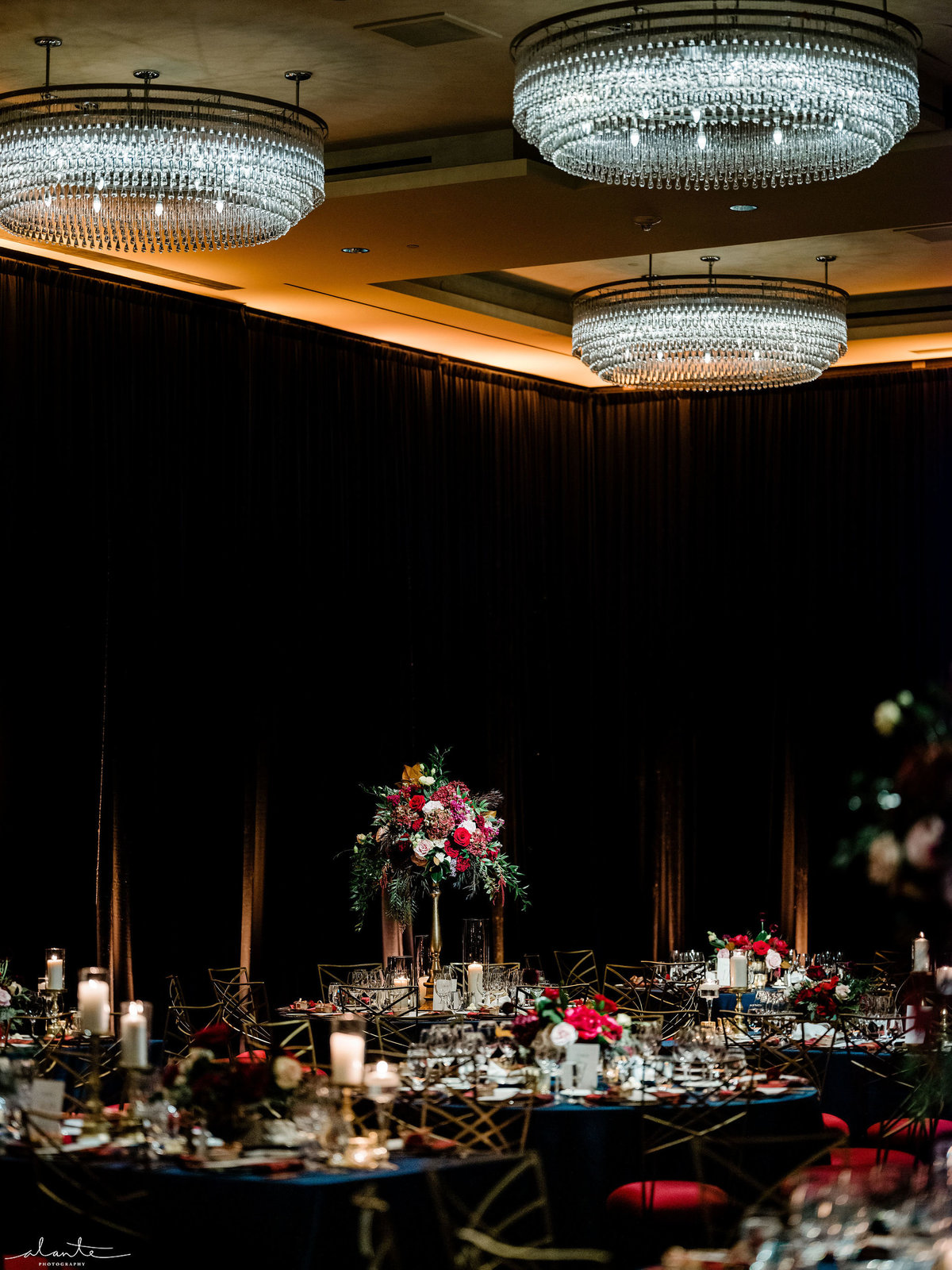 tall centerpiece of red and blush flowers in ballroom with navy blue draping, blue linens, and red seat Chameleon chairs