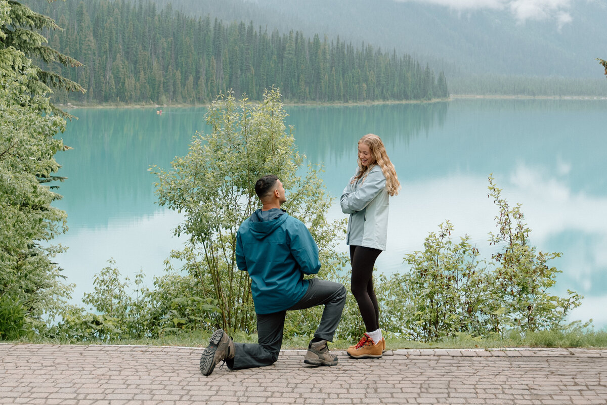 close up of man kneeling in front of girlfriend as he asks her to marry him in Emerald Lake. 