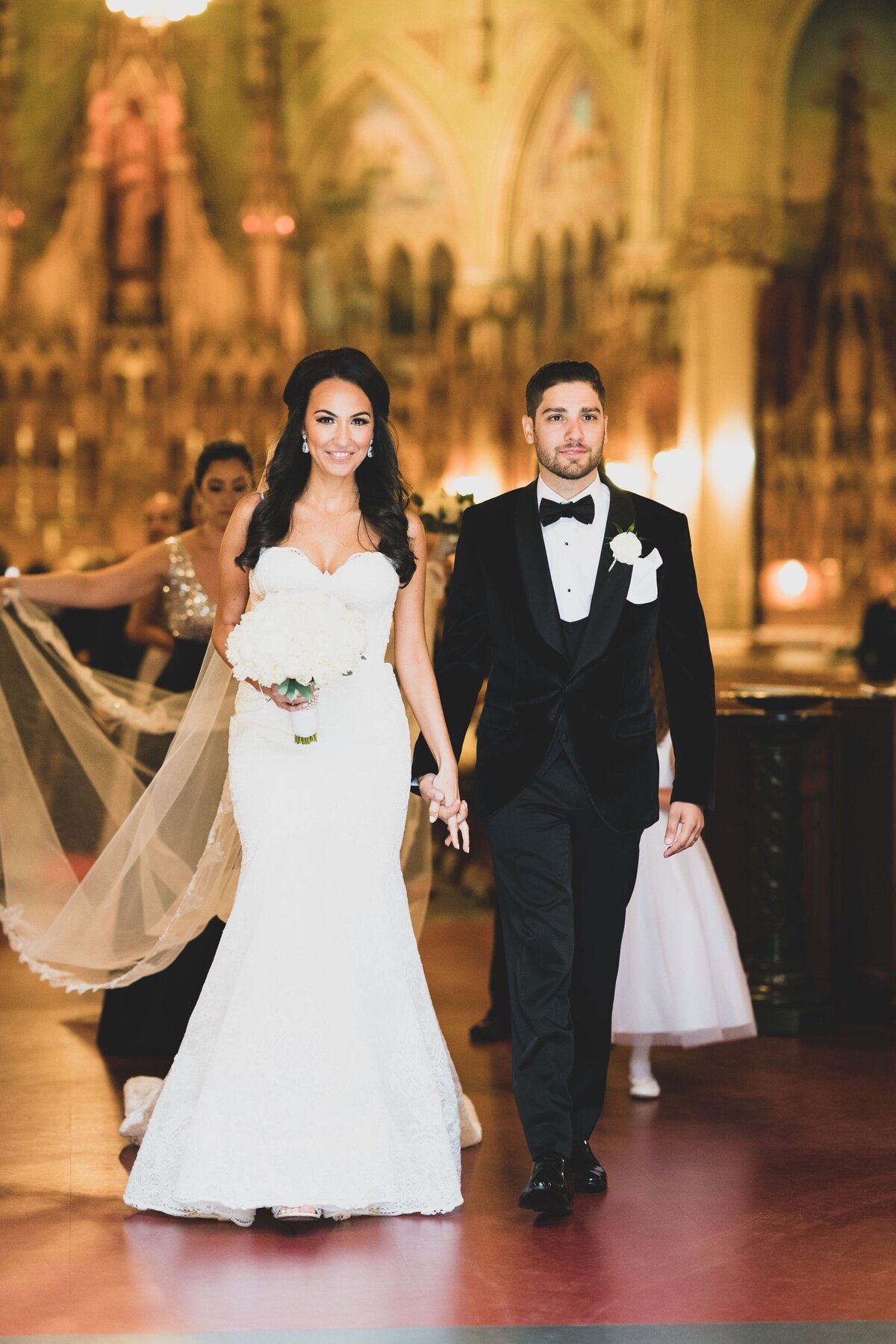 The couple walks down the aisle together, radiating happiness and anticipation. This image captures the emotional and ceremonial moment of their wedding procession, showcasing their unity and the significance of the occasion.