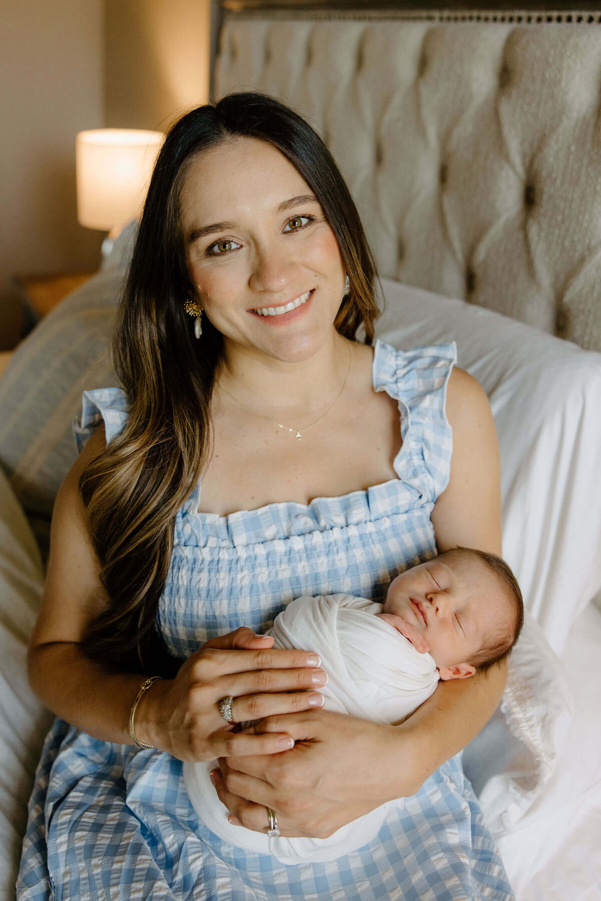 mother holding newborn son while sitting on edge of bed