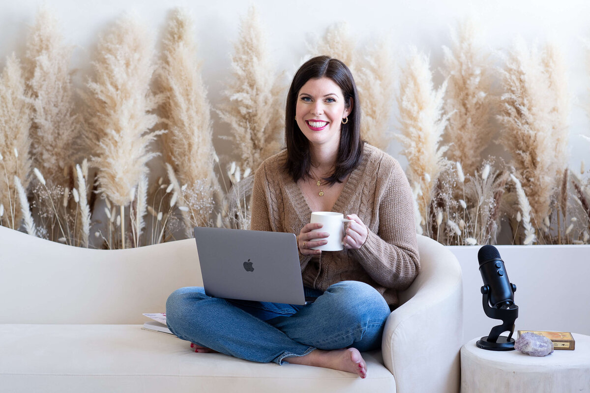 Ottawa branding photography of a woman in jeans sitting cross-legged on a couch smiling at the camera.