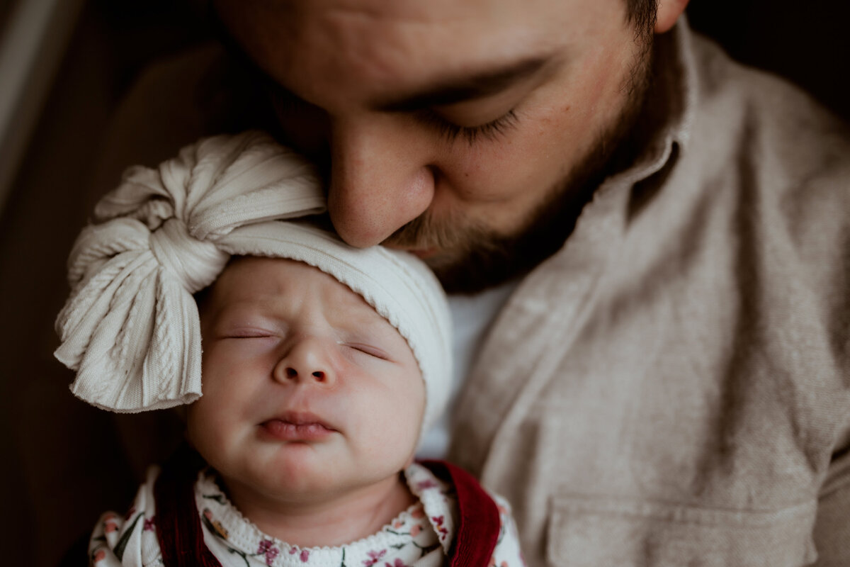 dad kisses top of newborn baby girl's head at lifestyle session