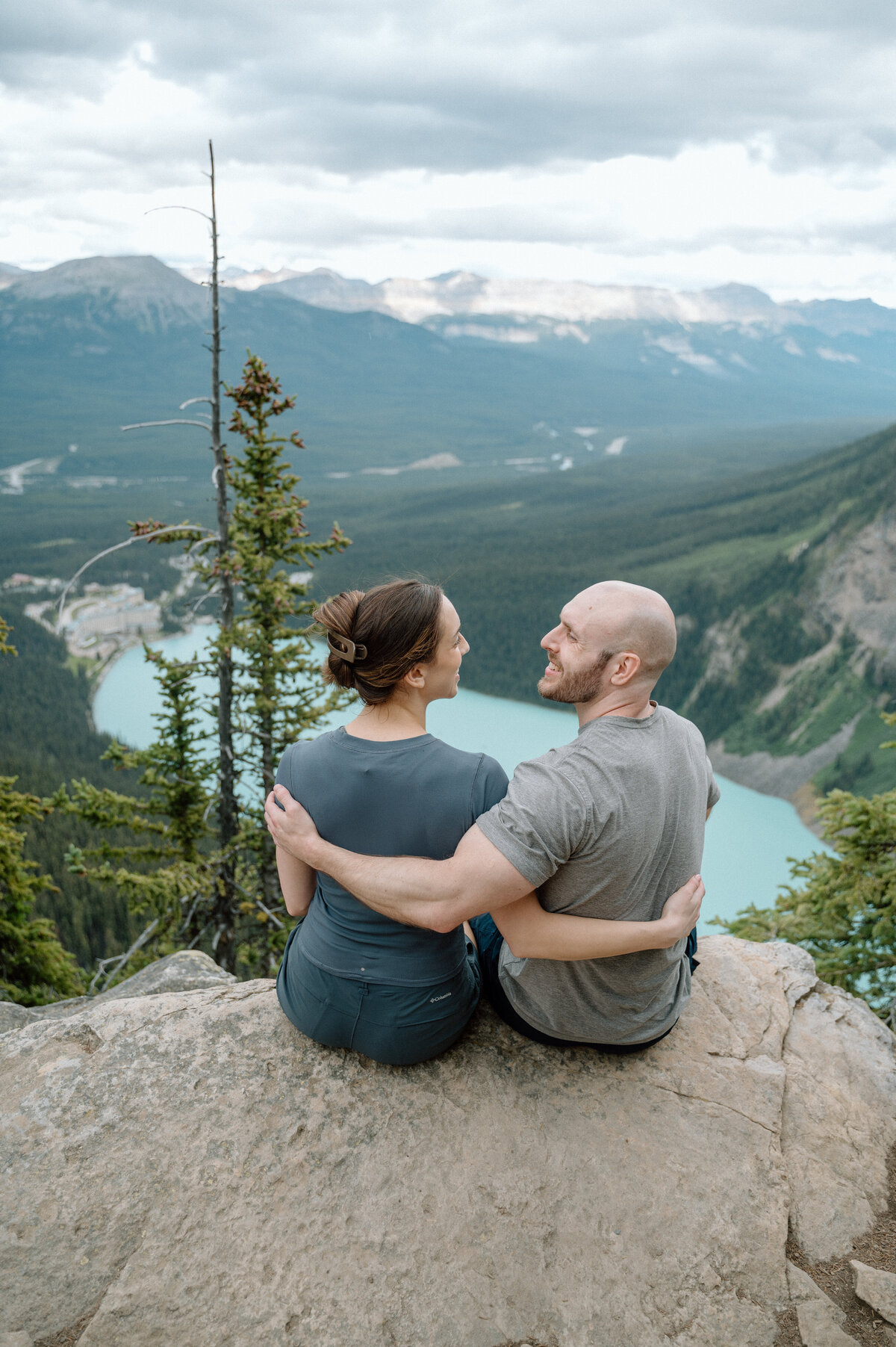 Snuggled couple with lake views at lake louise, captured during a stunning mountain proposal session.