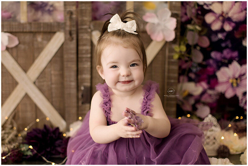 A baby girl claps during her purple cake smash