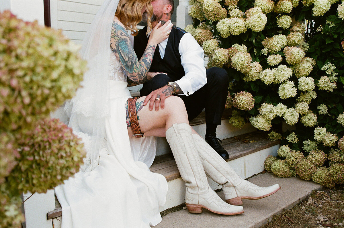 bride and groom sitting on step next to hydrangeas on their wedding day